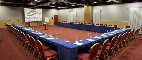 Ein Konferenzraum mit einem langen Tisch, roten Stühlen und einem Bildschirm, der 'SALAMANCA FORUM RESORT' anzeigt.