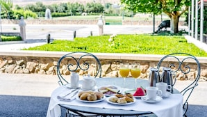 Une table dressée pour le petit-déjeuner, avec de la nourriture et des boissons, le tout mis en valeur par un décor pittoresque composé de verdure et d’un mur de pierres.