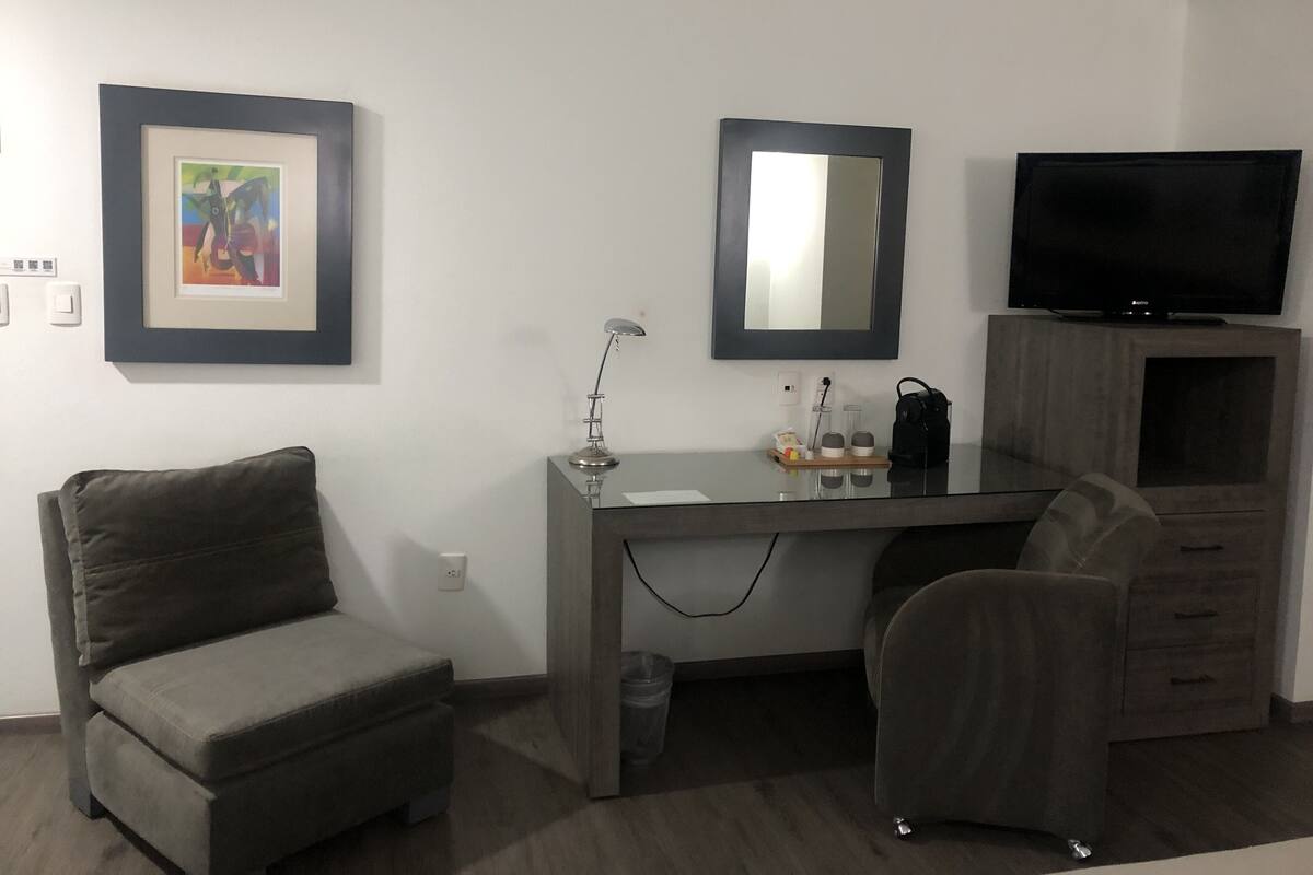 Een moderne kamer met een bureau, twee stoelen, een televisie en een lijst aan de muur.