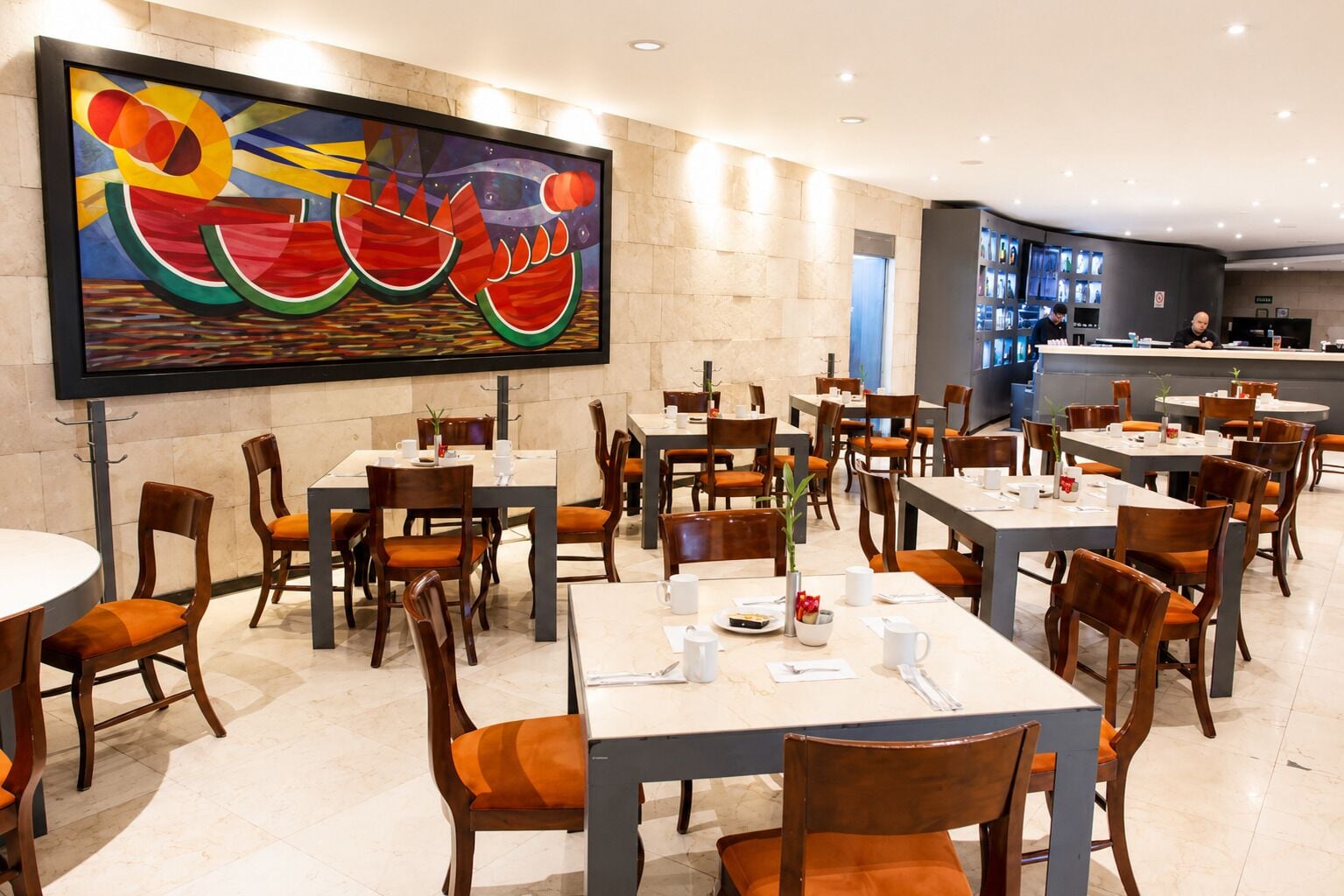 Un restaurante con varias mesas y sillas, un cuadro abstracto grande en la pared y una zona de barra al fondo.