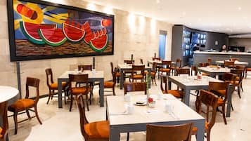 Un restaurante con varias mesas y sillas, un cuadro abstracto grande en la pared y una zona de barra al fondo.