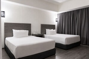 Een hotelkamer met twee bedden, een nachtkastje, een telefoon en een raam met gordijnen.