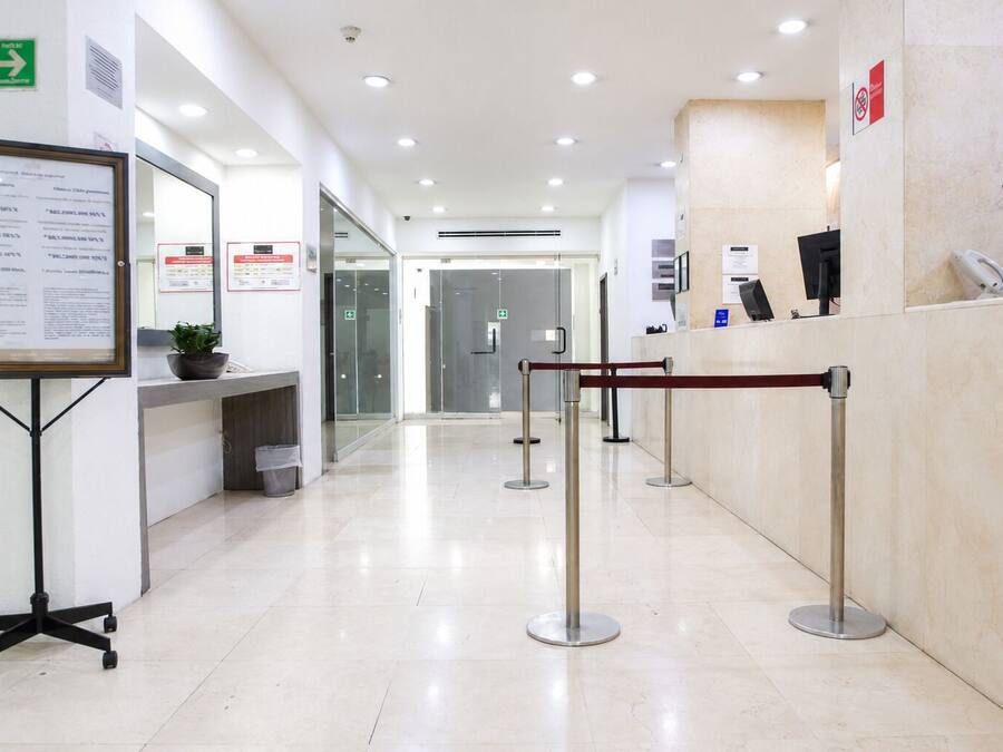 Un área de recepción limpia y bien iluminada, con mostrador de recepción, fila de espera y señalización informativa.