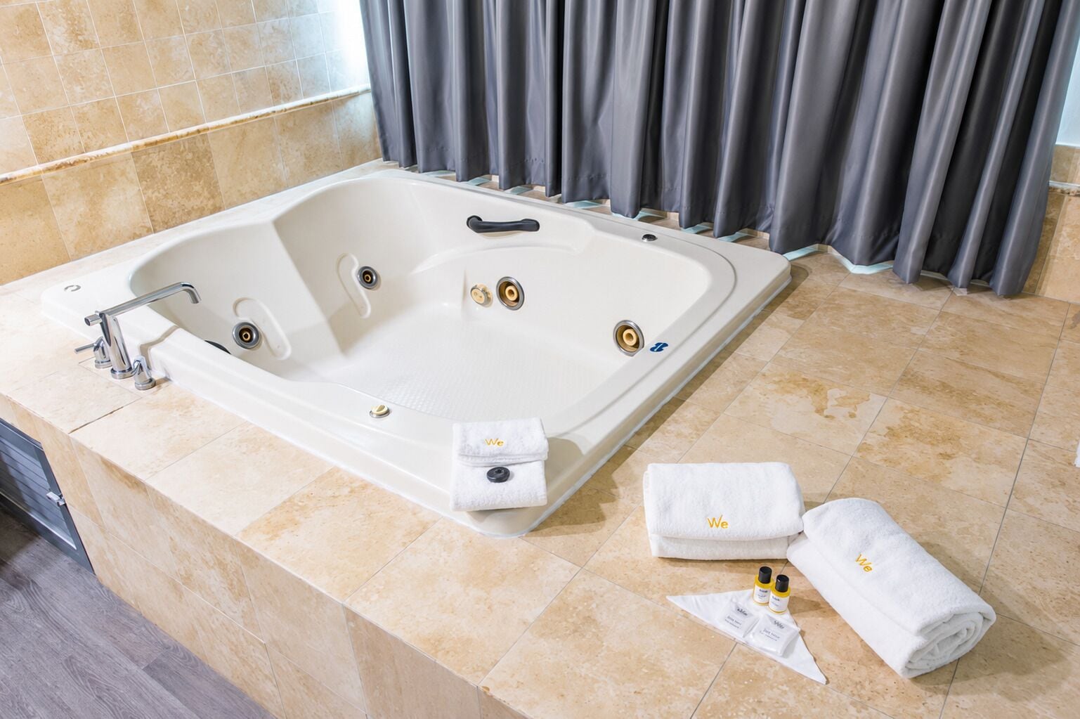 Una bañera blanca grande con una llave moderna, dos toallas y una botella de loción en el suelo.