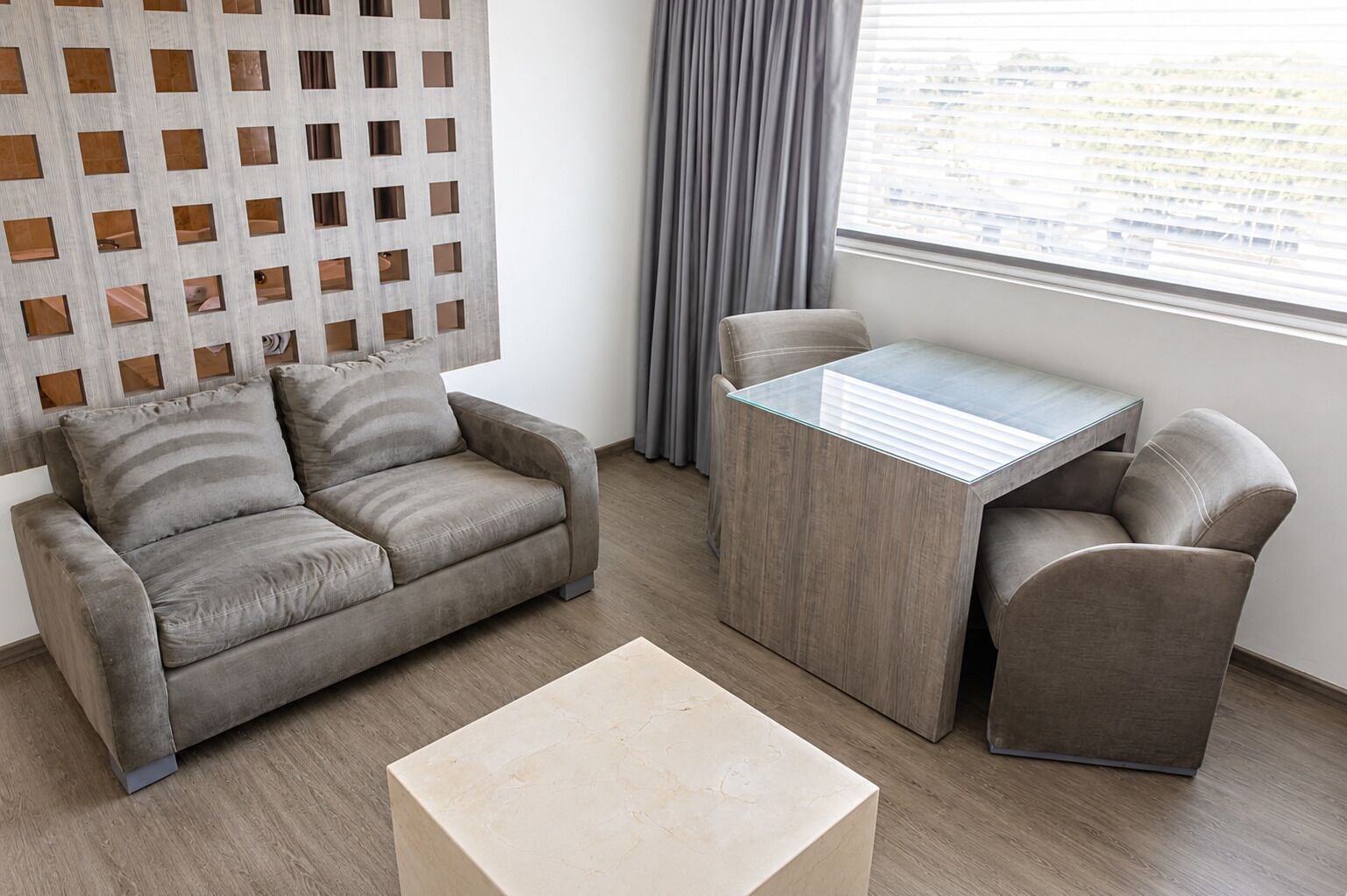 A modern living room with a sofa, two armchairs, a glass-top coffee table, and a decorative wall panel.