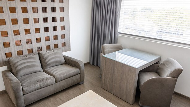 Ein modernes Wohnzimmer mit einer Couch, zwei Sesseln, einem Glastisch und einer dekorativen Wandverkleidung.