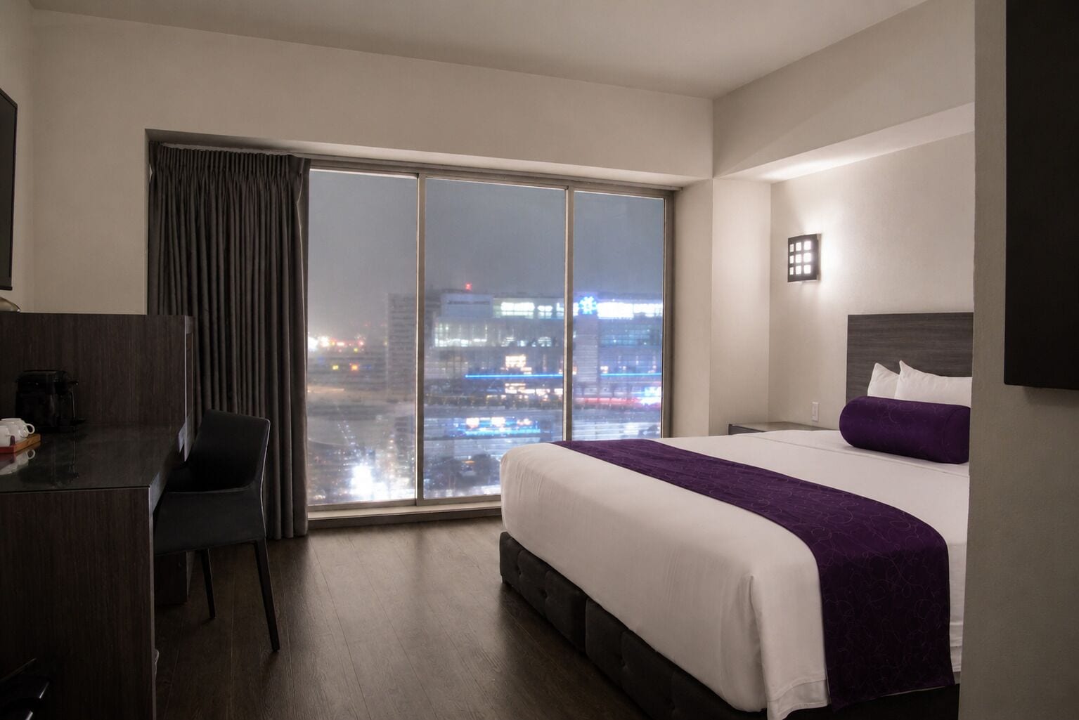 Una habitación de hotel con un ventanal grande, una cama, un escritorio y una silla.