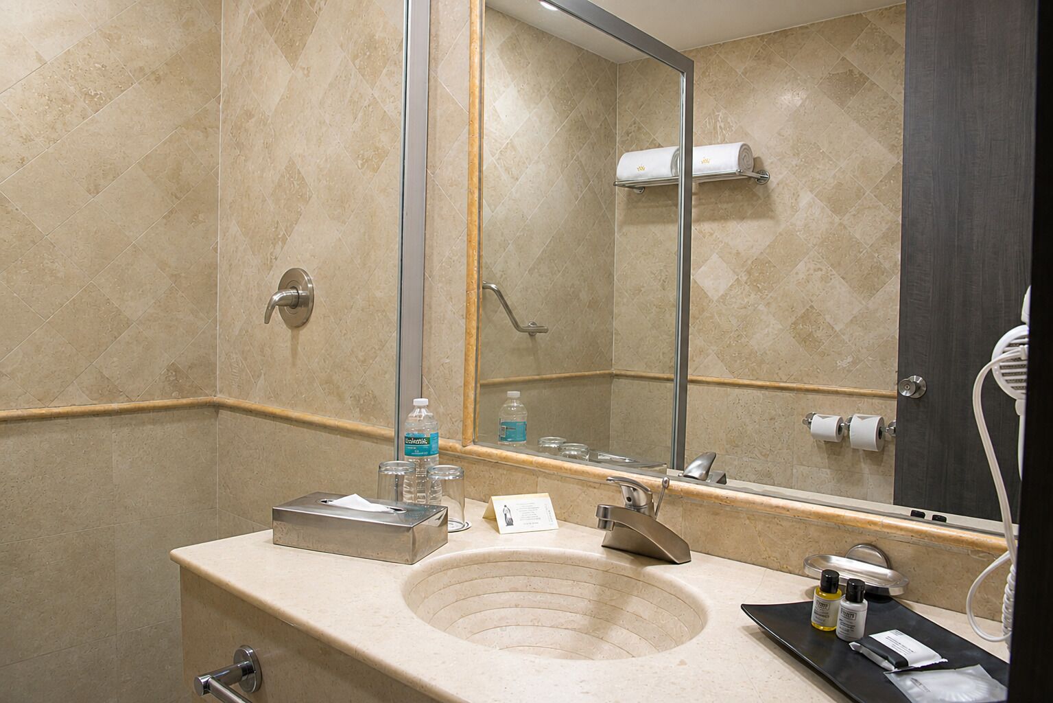 Un baño con lavamanos, espejo, toallero y artículos de aseo.