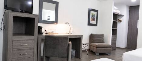 A hotel room with a desk, chair, bed, wardrobe, and a television.