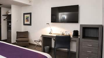 Habitación de hotel con cama, escritorio, silla, televisor, armario y cubo de basura.