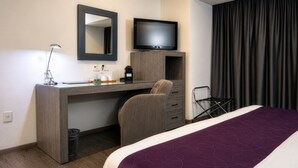 Ein Hotelzimmer mit Bett, Schreibtisch mit Stuhl, Fernseher und einem Fenster mit Vorhängen.