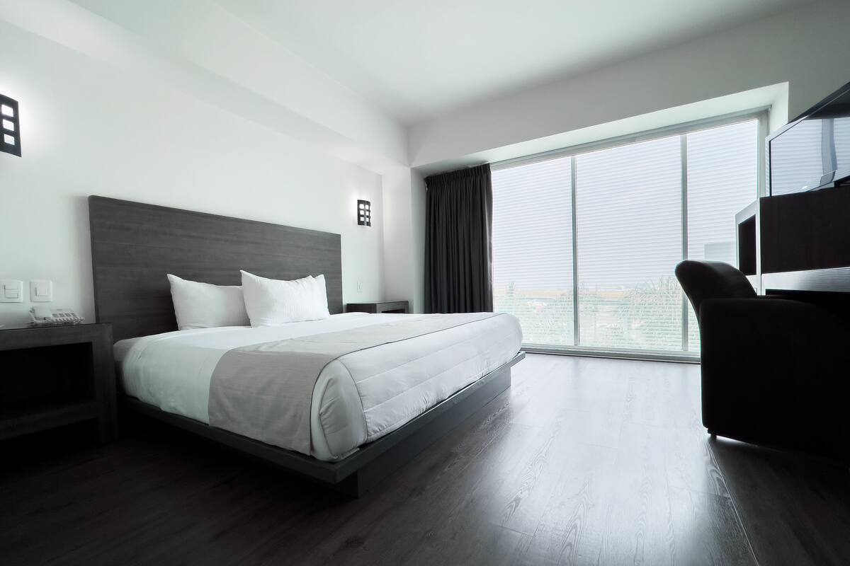 Een moderne hotelkamer met een groot bed, een bureau, een stoel en een groot raam met uitzicht.