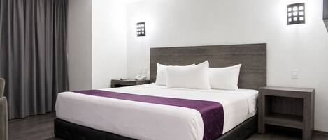 Habitación de hotel con una cama grande, una mesita de noche, una silla y una ventana con cortinas.
