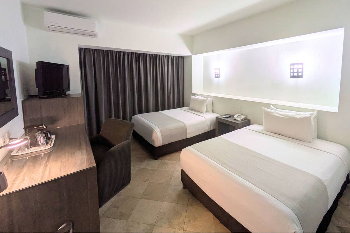 Een hotelkamer met twee bedden, een bureau met een televisie, telefoon en een minibar.