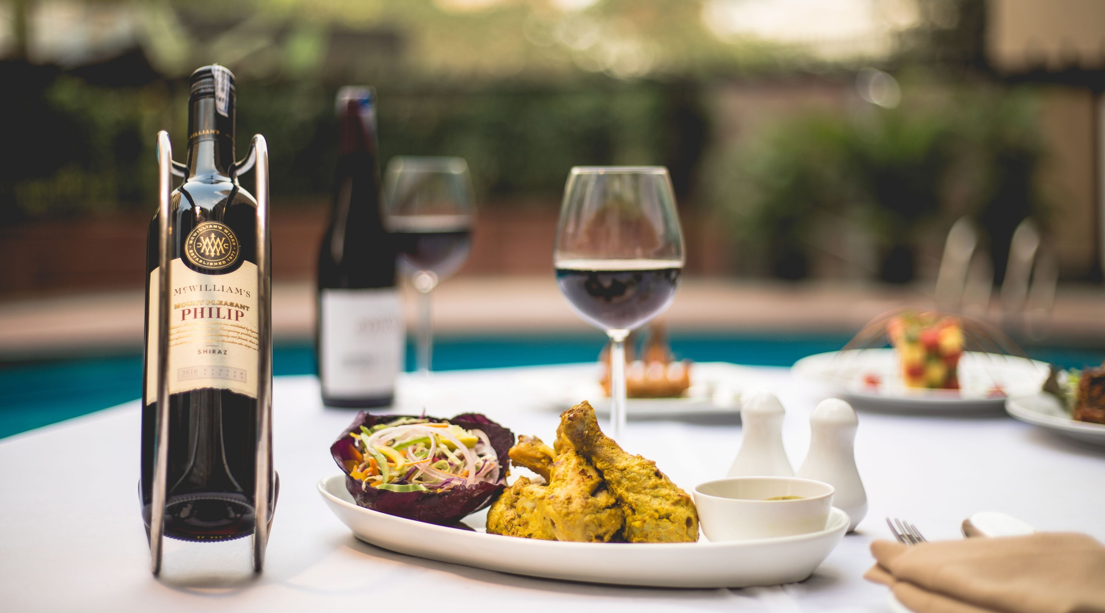 Una mesa de comedor con una botella de vino, una copa de vino y platos de comida.