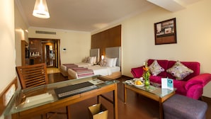 A hotel room with two beds, a red sofa, a glass table, and a wooden chair. - The Chancery Pavilion (Bengaluru)