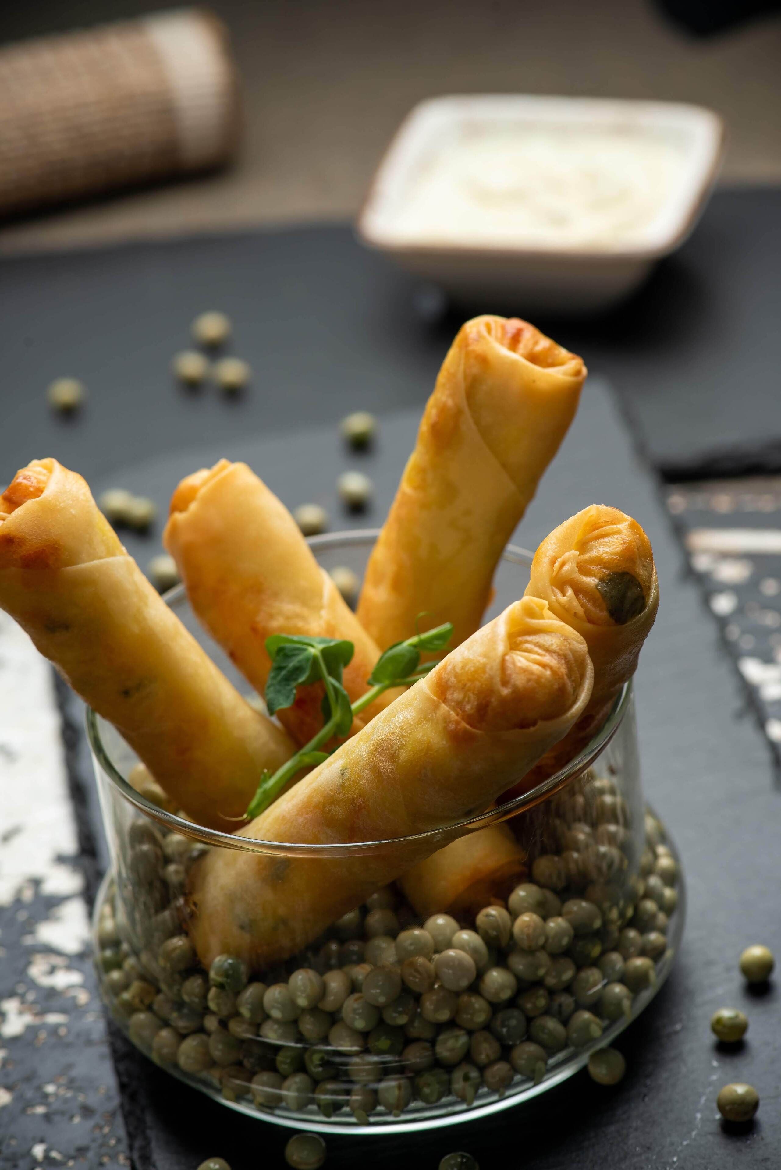 A glass bowl containing spring rolls and a small bowl of dipping sauce.