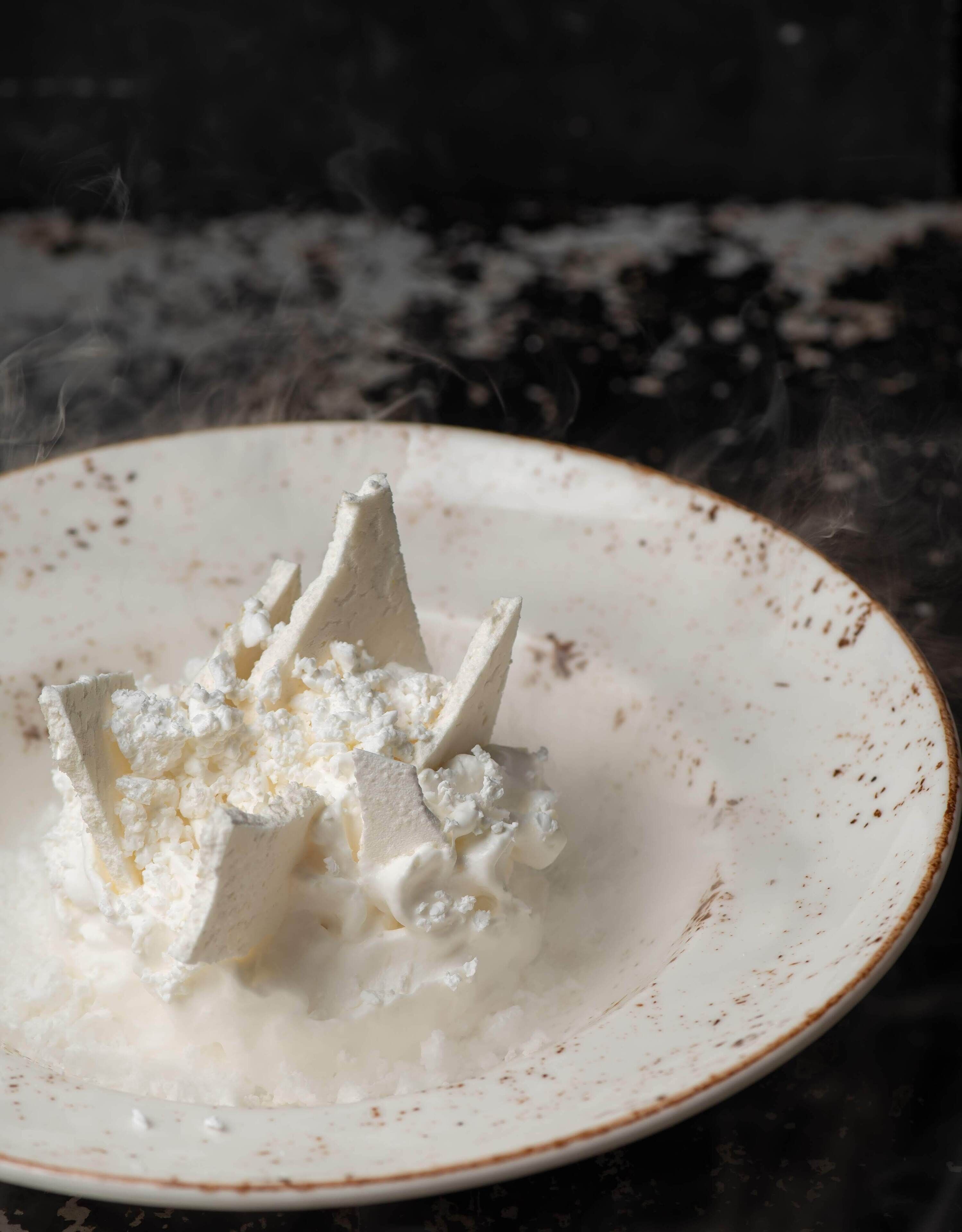 A white plate with a pile of white, crumbly substance, possibly cheese or a similar food item, on a dark surface.