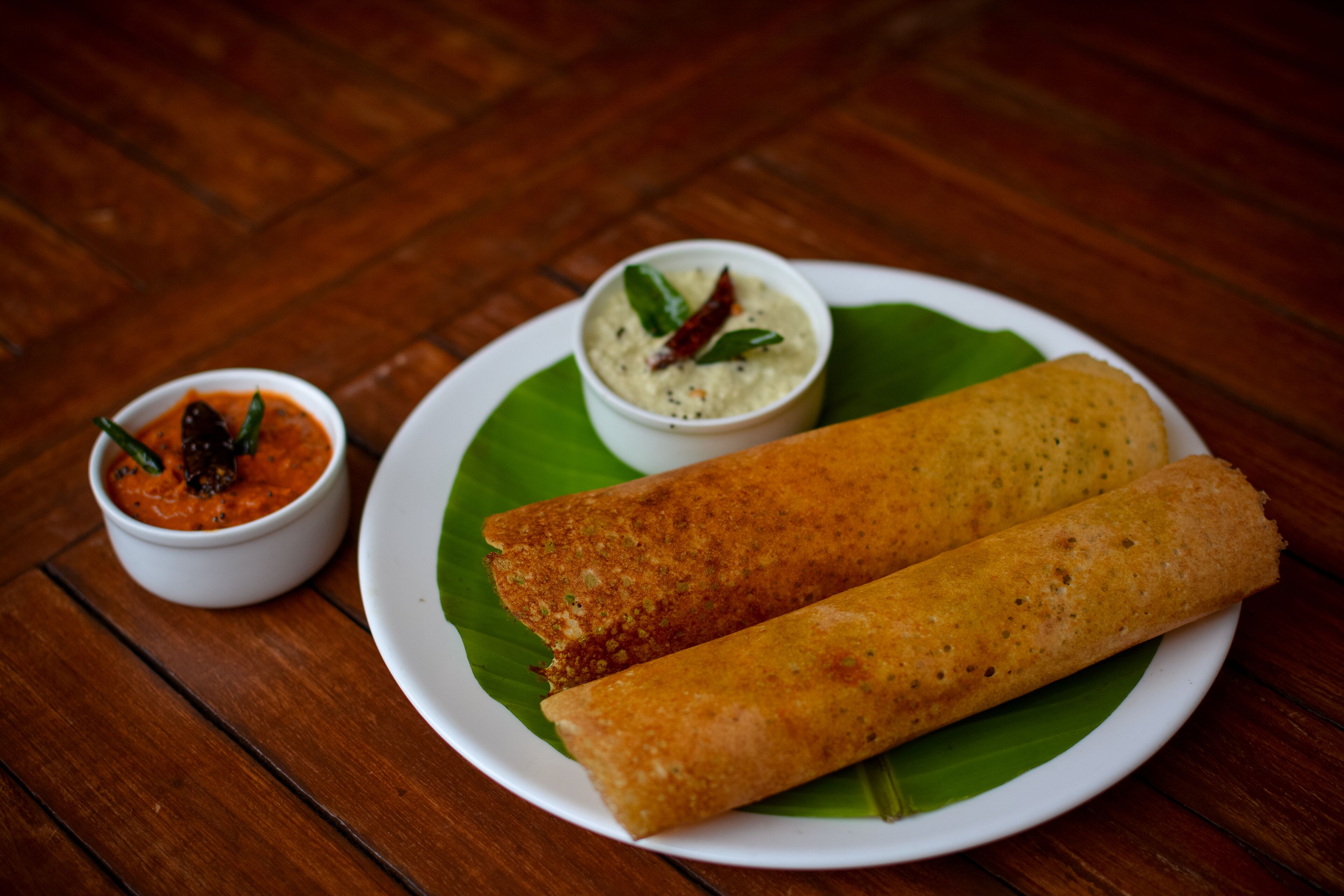 A plate with two rolled items, possibly a type of flatbread, and two small bowls of sauce or dip on a wooden table.
