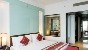 A hotel room with a large bed, a nightstand, a mirror, and a view of the bathroom. - The Chancery Pavilion (Bengaluru)