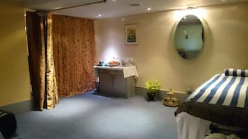 A hotel room with a bed, a small desk with a mirror, a potted plant, and a window with curtains.