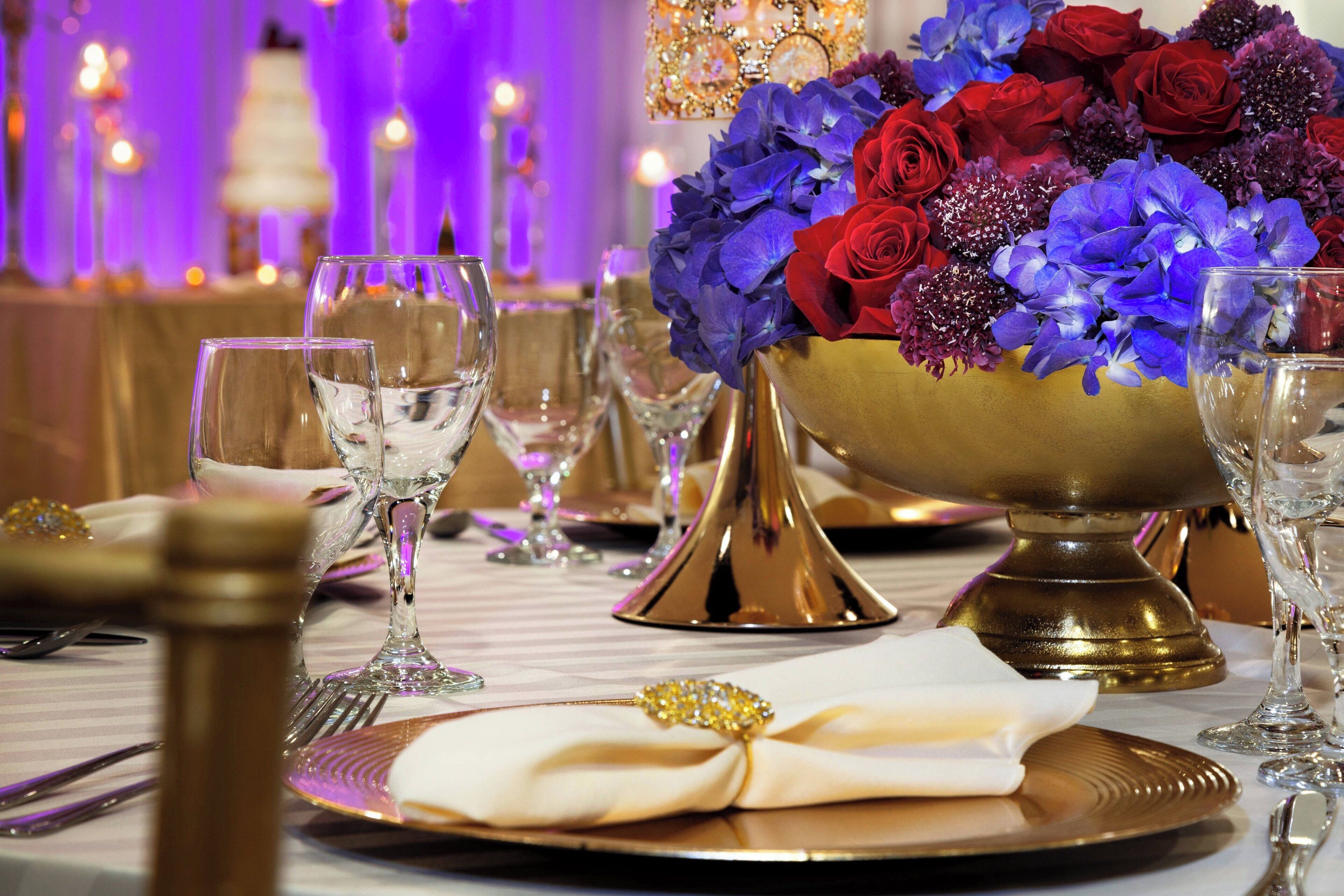 Ein Tisch ist mit feinem Porzellan, Kristallgläsern und einem Blumenarrangement in Rot und Blau gedeckt.