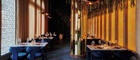 A restaurant with tables set for dining, a large mirror, and a decorative wall with hanging plants.