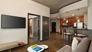 A modern living room with a sofa, a coffee table with books and apples, a bench, and a flat-screen TV mounted on the wall. - Twelve Midtown, Autograph Collection (Atlanta)