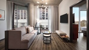 A modern living room with a sofa, a round table, and a TV mounted on the wall. - Twelve Midtown, Autograph Collection (Atlanta)