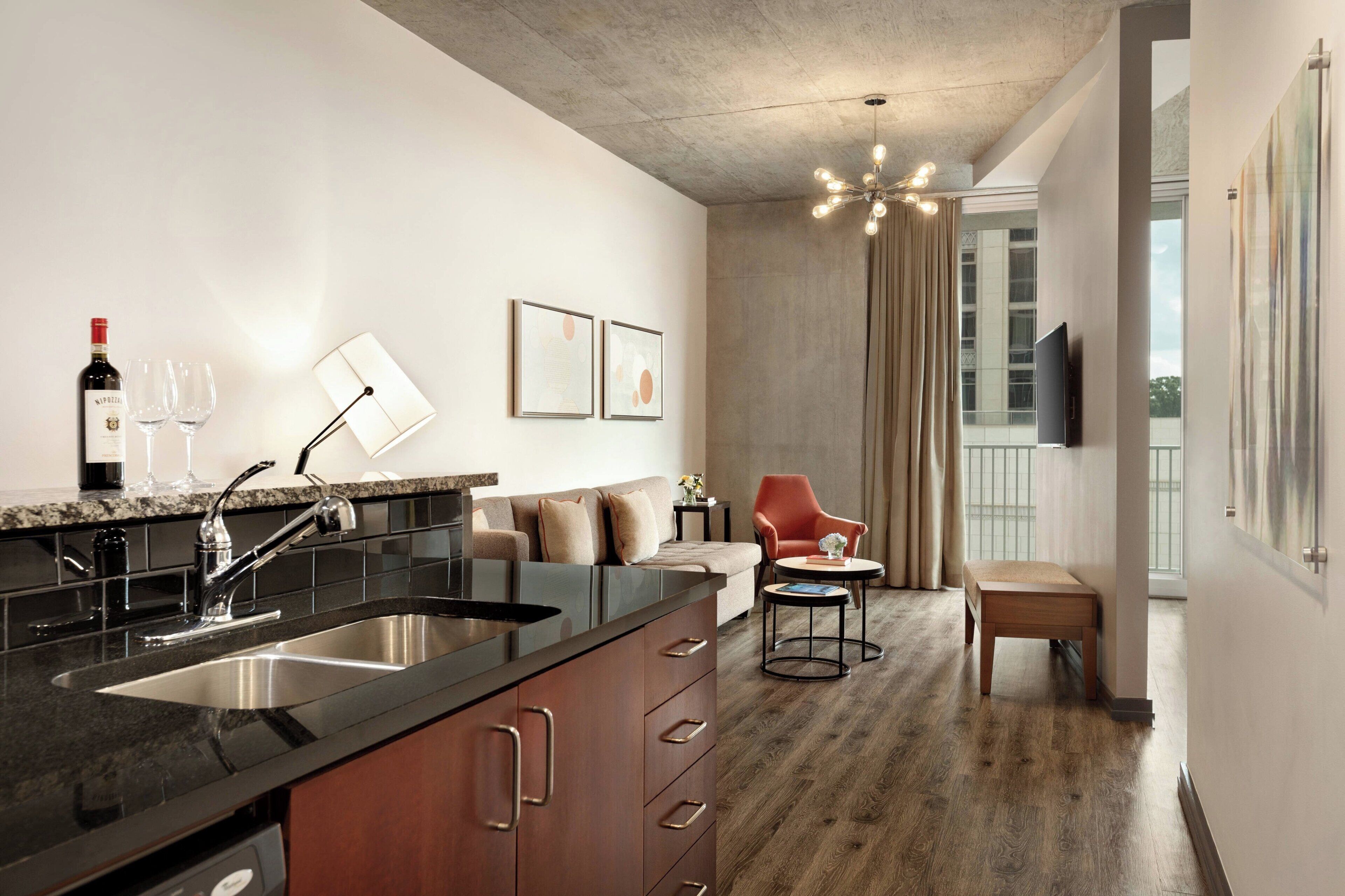 A modern kitchen with a built-in sink, a dining area with a red chair, and a large window with curtains.