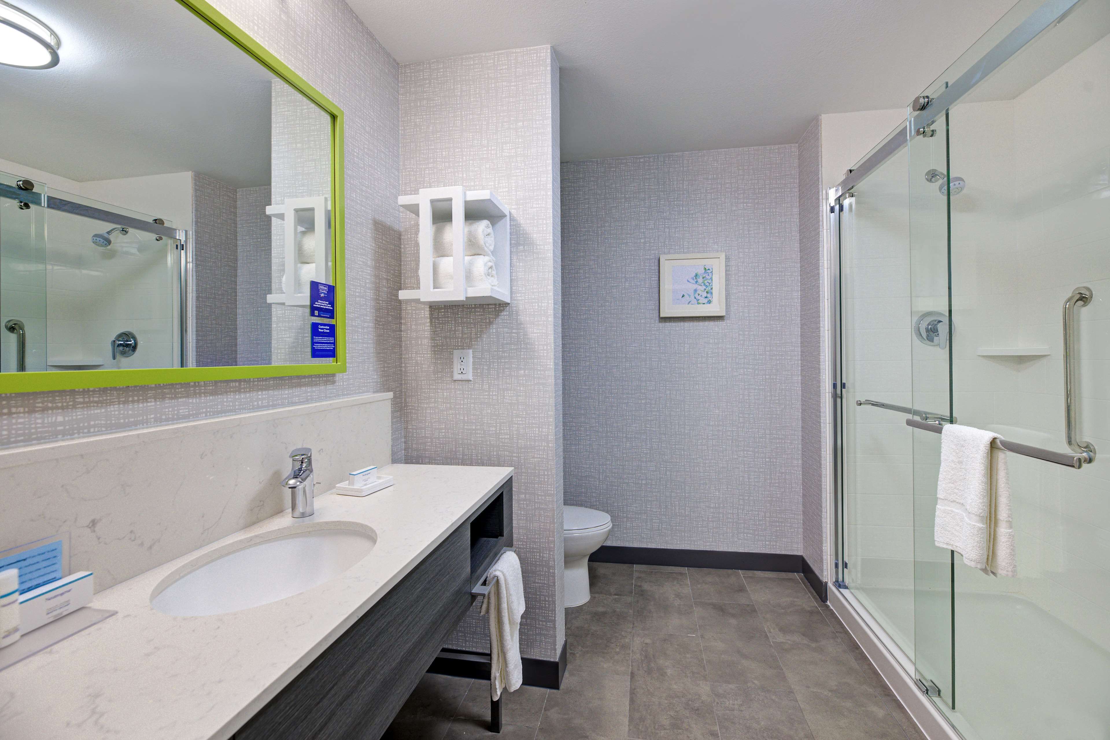 Un baño moderno con ducha de vidrio, lavamanos con espejo y un inodoro.