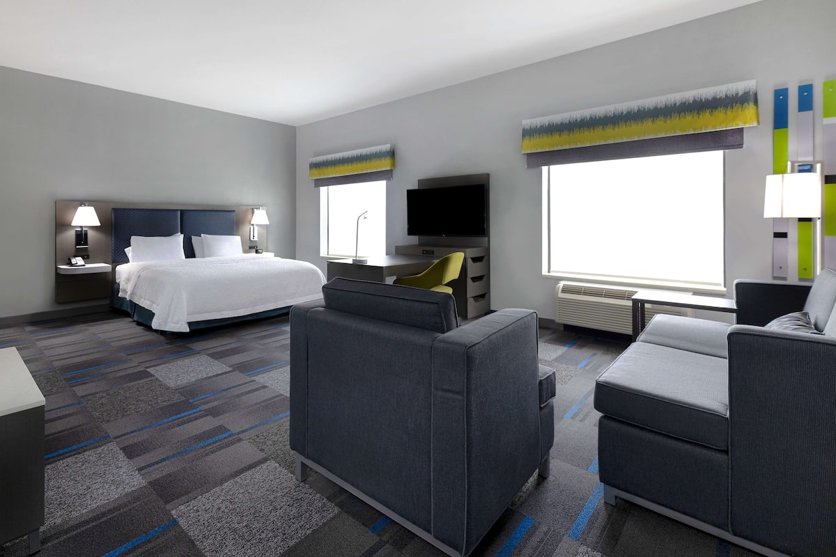 A hotel room with a bed, a desk, a TV, and a seating area.
