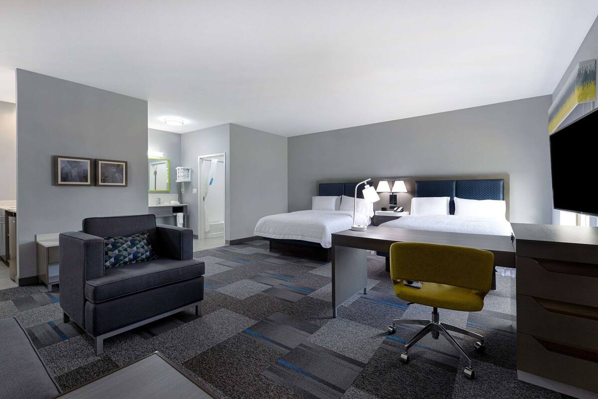 A hotel room with a bed, desk, chair, and a small kitchenette.