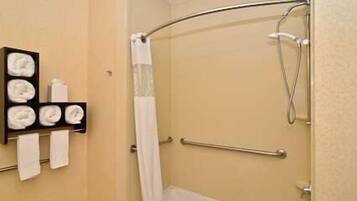 A corner shower with a curved glass door, a towel rack with folded towels, and a grab bar for safety.