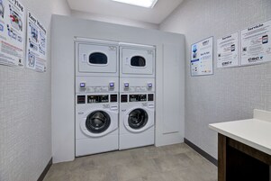 Un cuarto de lavandería con lavadoras y secadoras apiladas, paneles de control y carteles informativos en las paredes.
