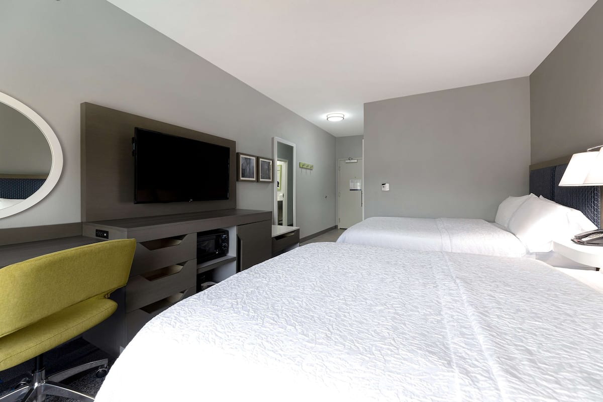 A hotel room with a bed, a desk with a chair, a television, and a mirror.