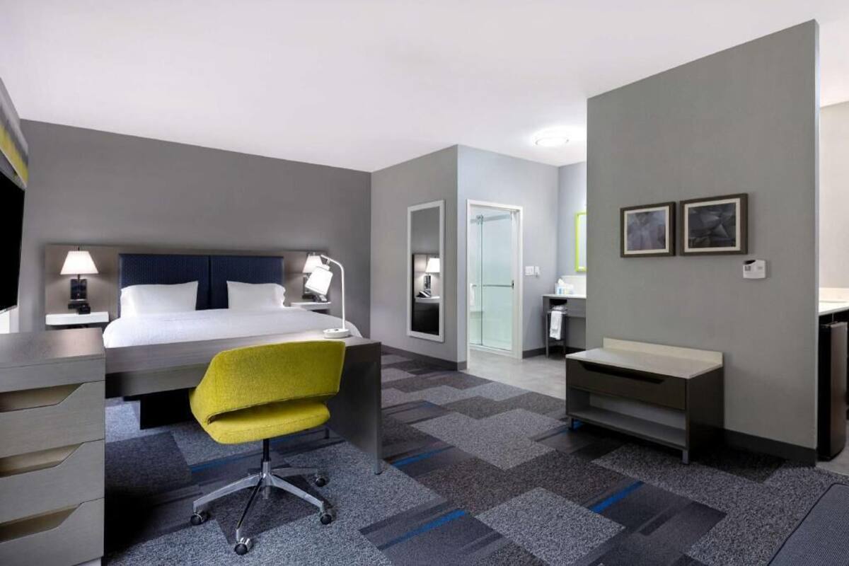 A hotel room with a bed, desk, chair, and a small bathroom area.