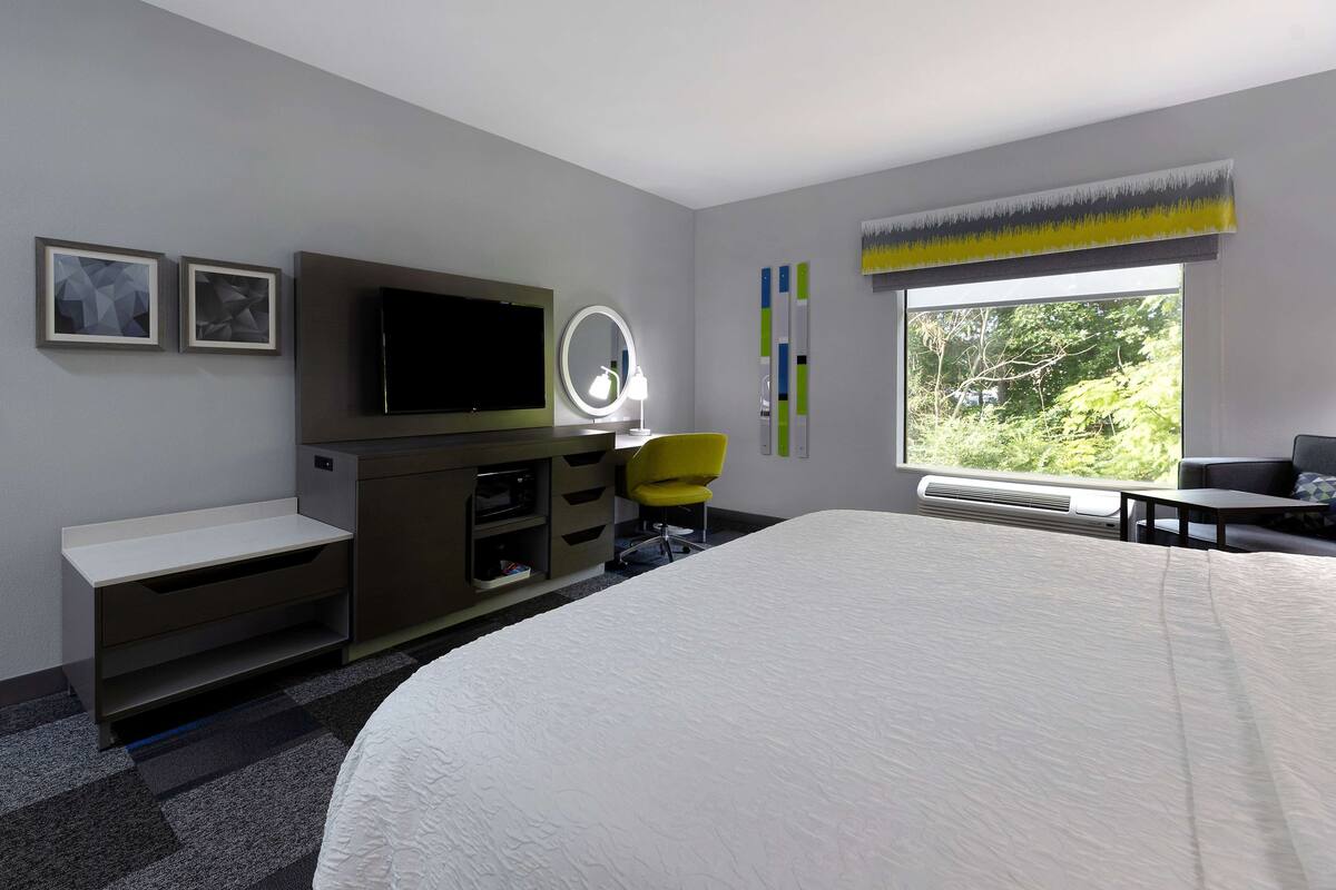 A modern hotel room with a large bed, a flat-screen TV, a vanity with a mirror, a desk, and a chair.