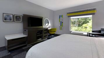 A modern hotel room with a large bed, a flat-screen TV, a vanity with a mirror, a desk, and a chair.