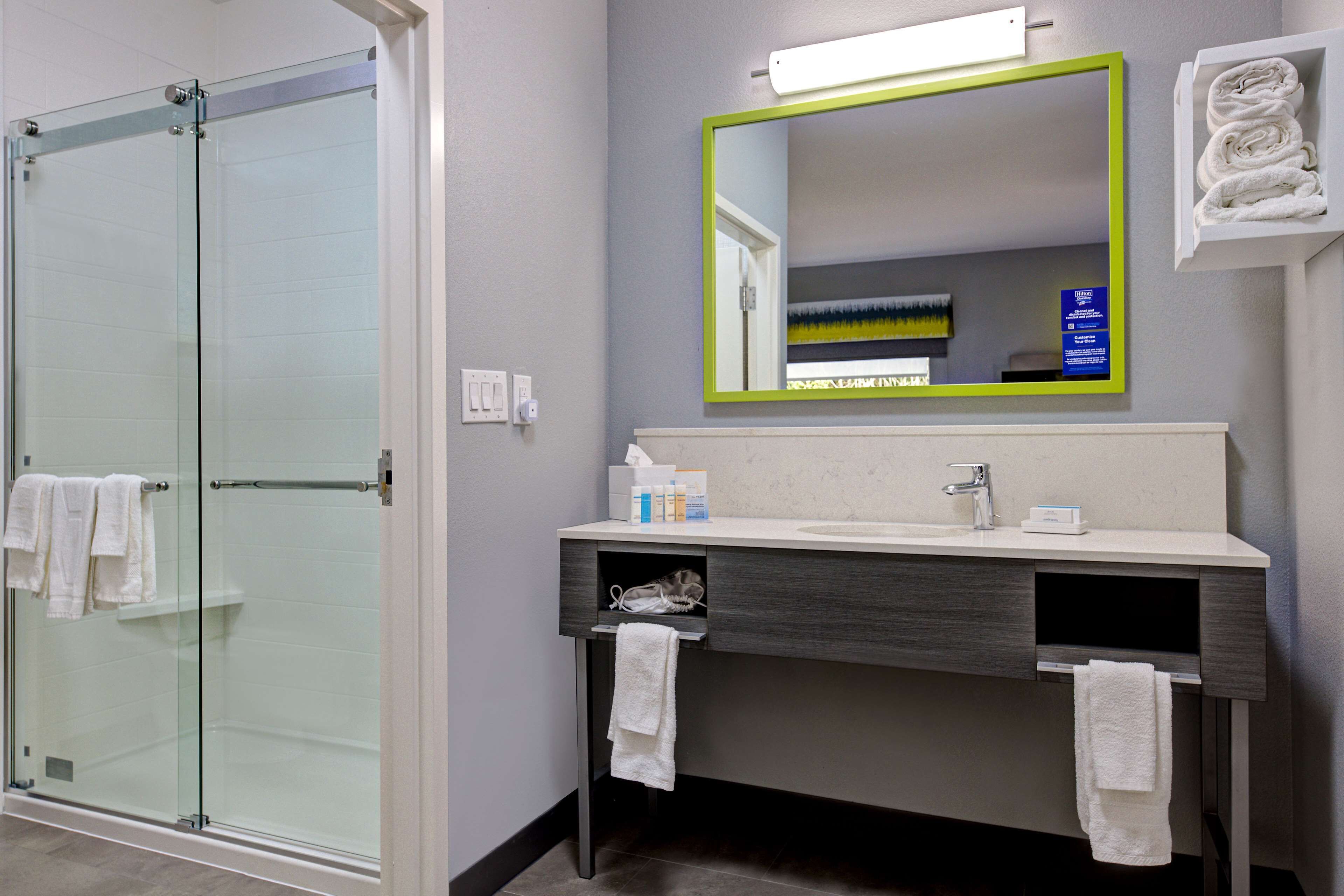 A bathroom with a glass shower enclosure, a sink with a mirror, and towels on the wall.