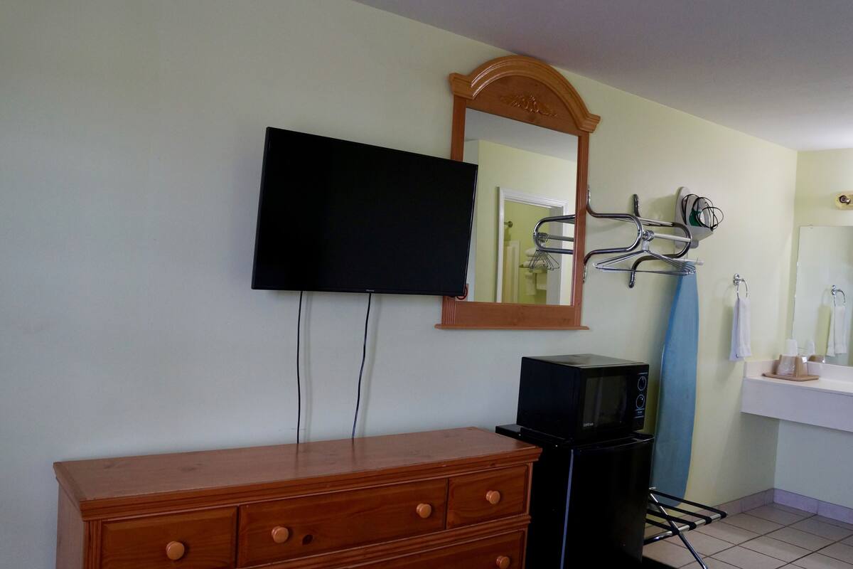 Una habitación con un aparador de madera, un televisor de pantalla plana montado en la pared, un microondas y una tabla de surf apoyada contra la pared.