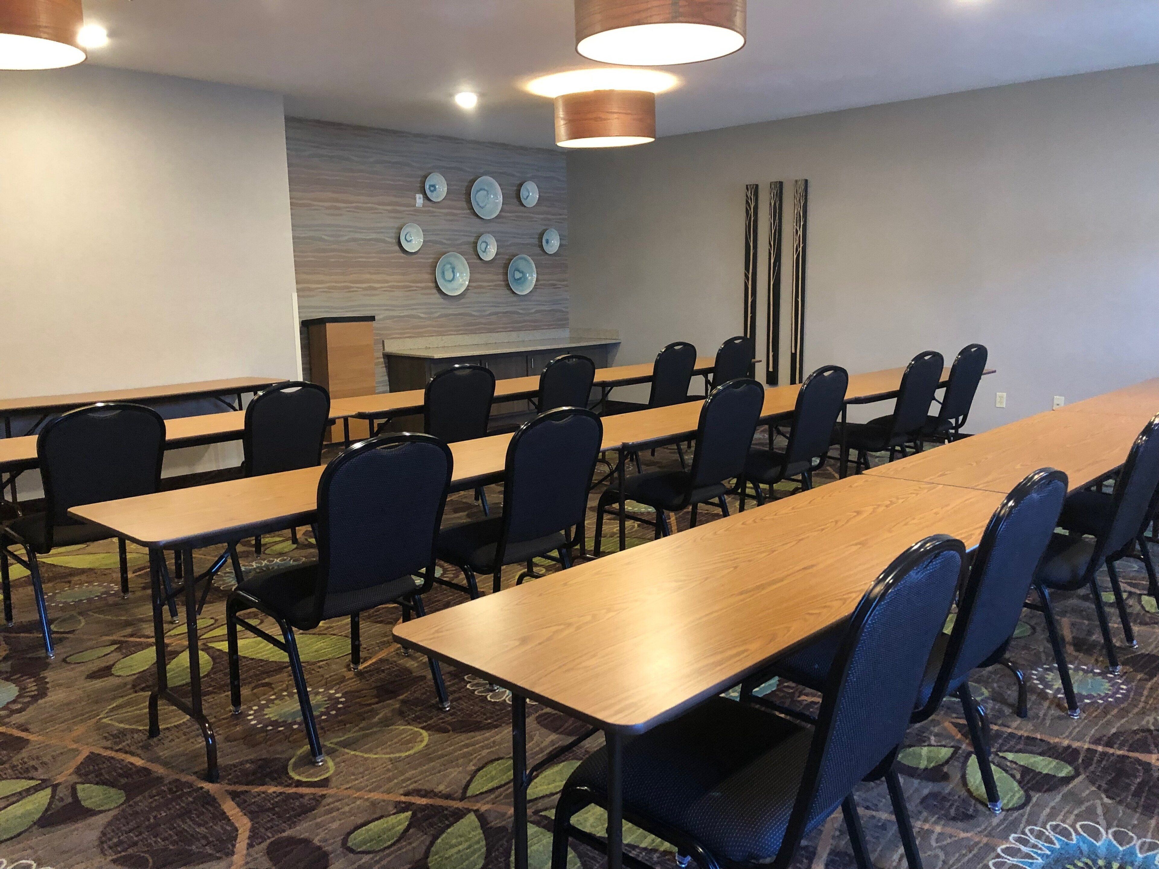 Een congreszaal met lange tafels en stoelen, een kamerbreed tapijt met patroon en wanddecoratie.