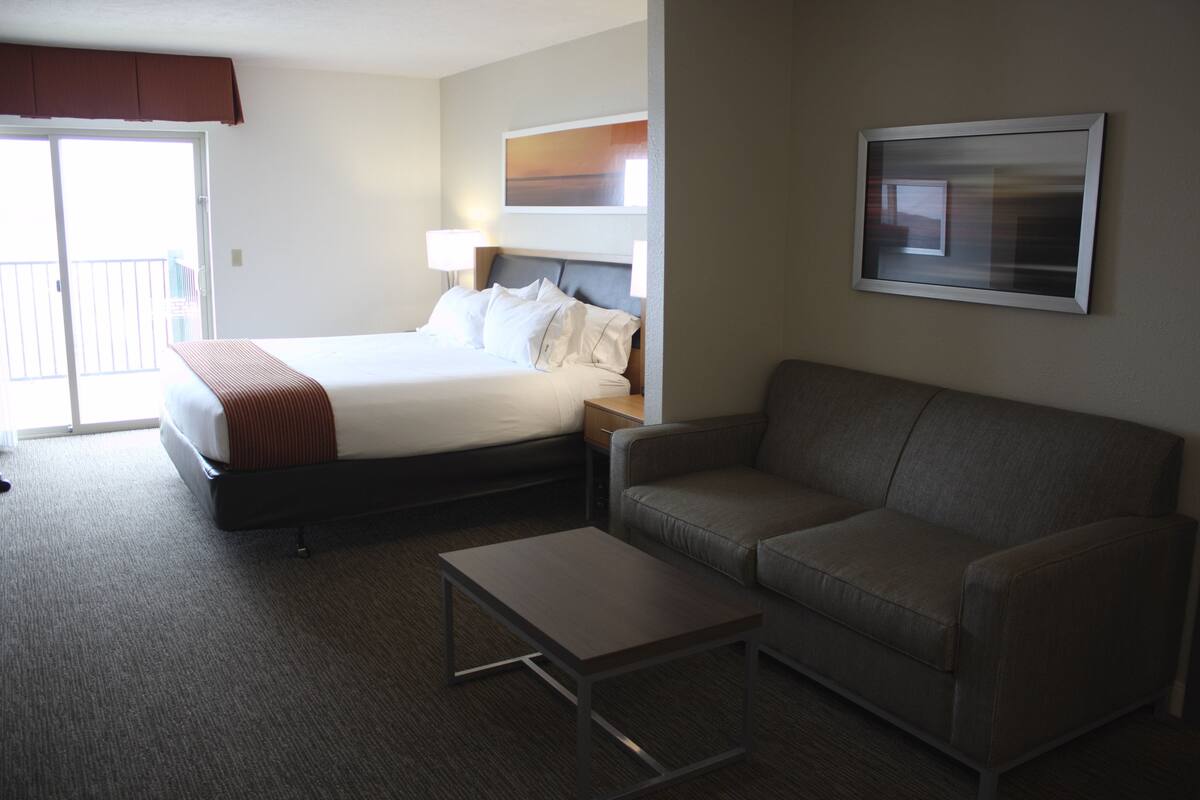 A hotel room with a bed, a sofa, a coffee table, a lamp, and a painting on the wall.