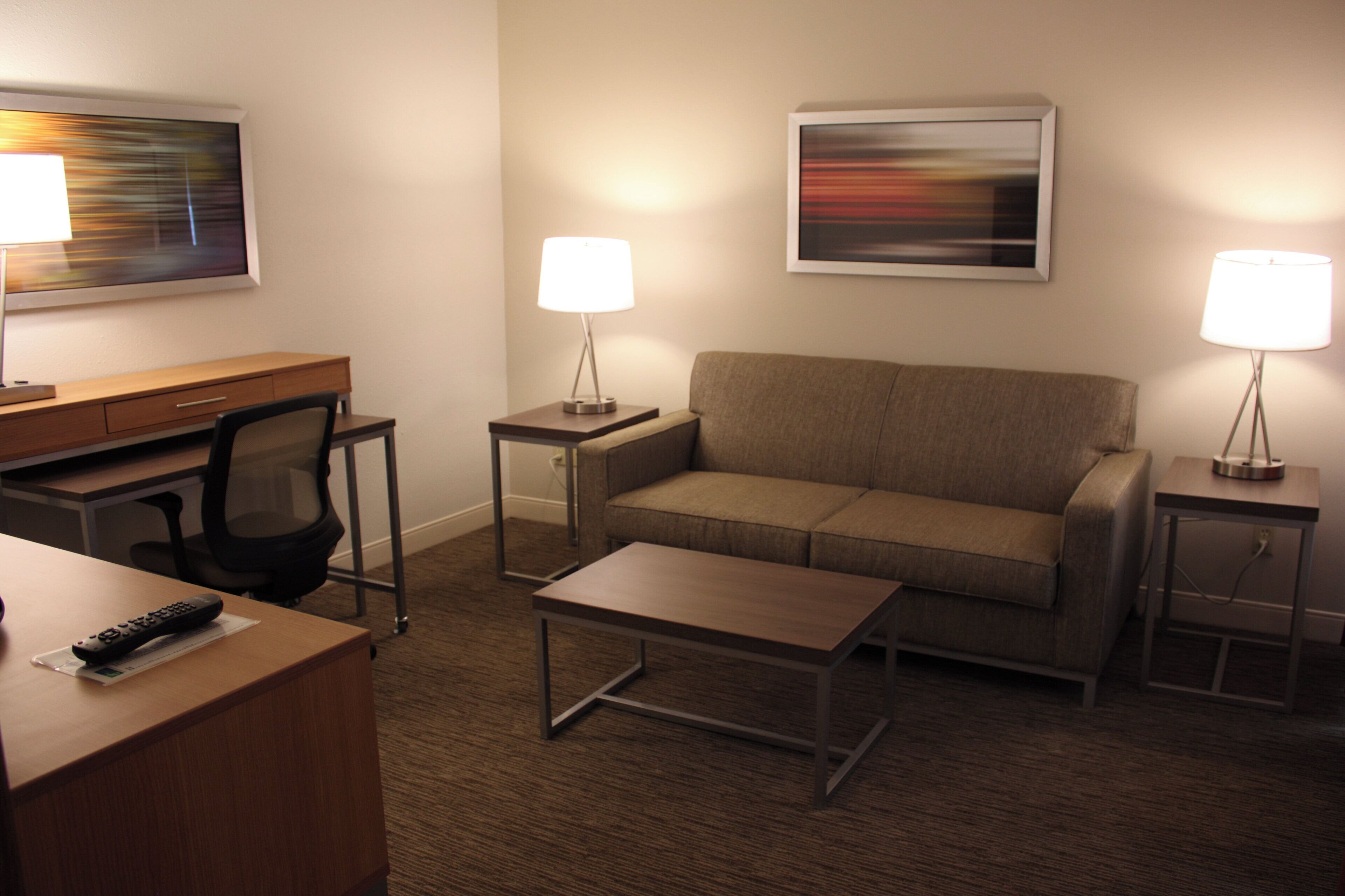 A hotel room with a desk, office chair, sofa, and two side tables with lamps.