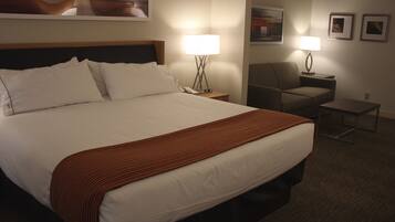 A hotel room with a large bed, two bedside tables with lamps, a chair, and a small table.