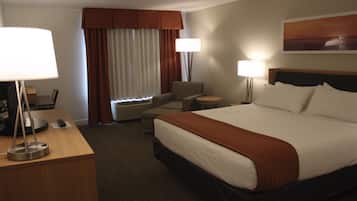 Habitación de hotel con una cama grande, dos lámparas de noche, un escritorio con lámpara, una silla y una ventana con cortinas.