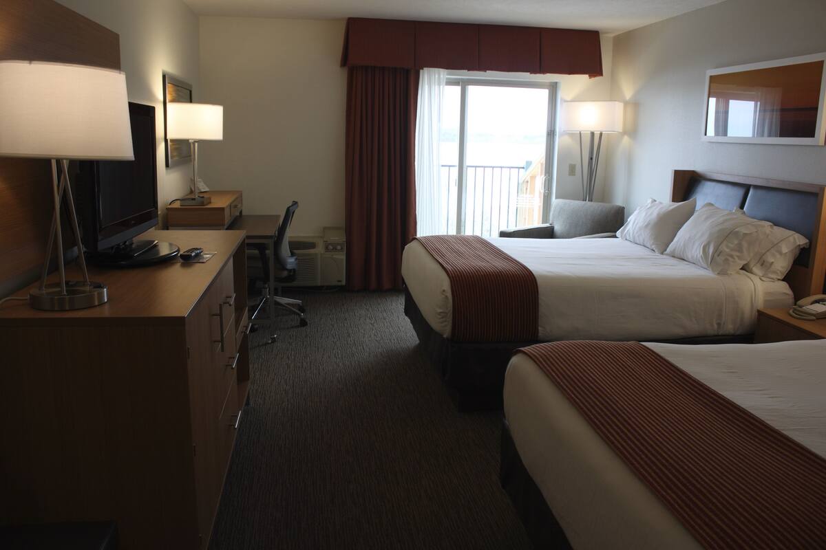 A hotel room with two beds, a desk with a computer, a TV, and a window with curtains.