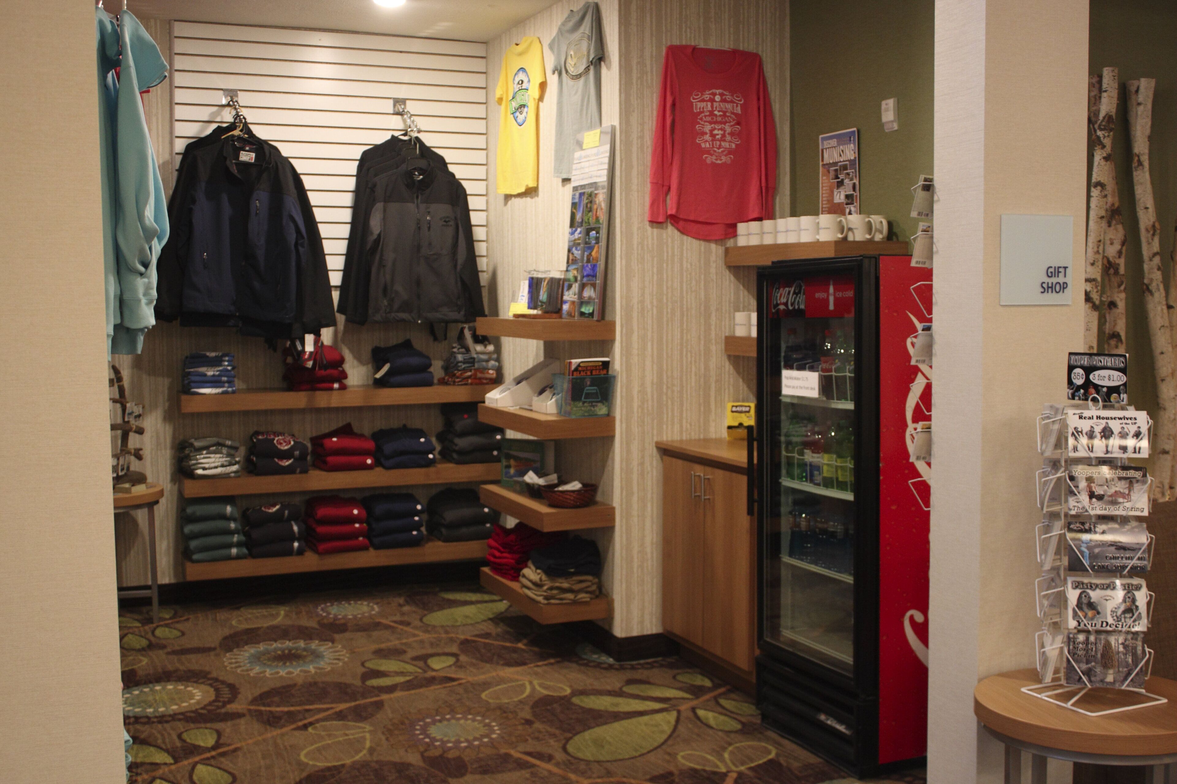 A retail space with shelves of folded clothing, a refrigerator, and a display of postcards.