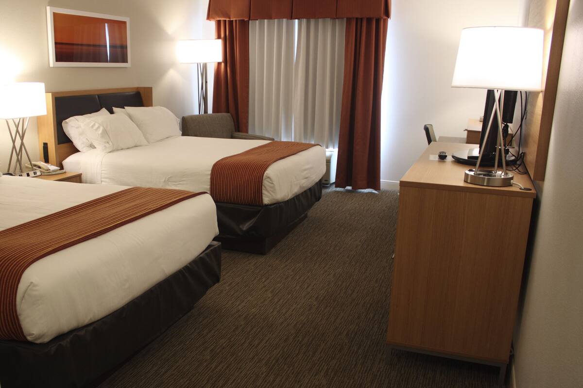 A hotel room with two beds, a desk, a lamp, and a telephone.