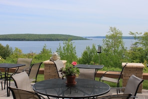 An outdoor patio with round tables and chairs, a stone wall, and a view of a lake and forest. - Holiday Inn Express Munising-Lakeview by IHG (Munising)